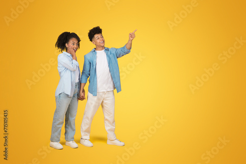A joyful young woman and man hold hands, with the man pointing and looking away in excitement