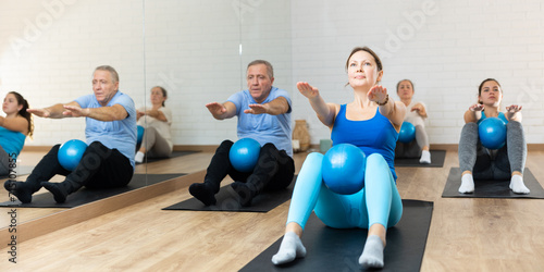 Canvastavla Slim middle-aged woman engaging in pilates training with ball in gym room during workout session
