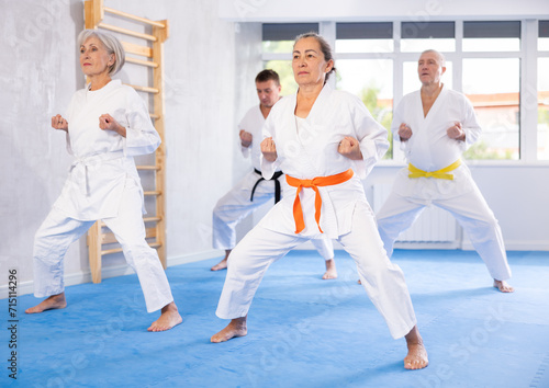 Active mature woman wearing kimono training karate techniques in group during workout session
