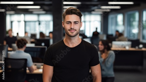 A businessman wearing a plain black T-Shirt stood in an office with a blurred background