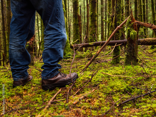 Tourist in blue jeans and tough brown leather outdoor boots on a green moss in a dense forest. Trip to nature and outdoor activity concept.