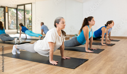 Concentrated senior woman practicing yoga positions during group training in fitness center, performing back bending asana Urdhva Mukha Shvanasana