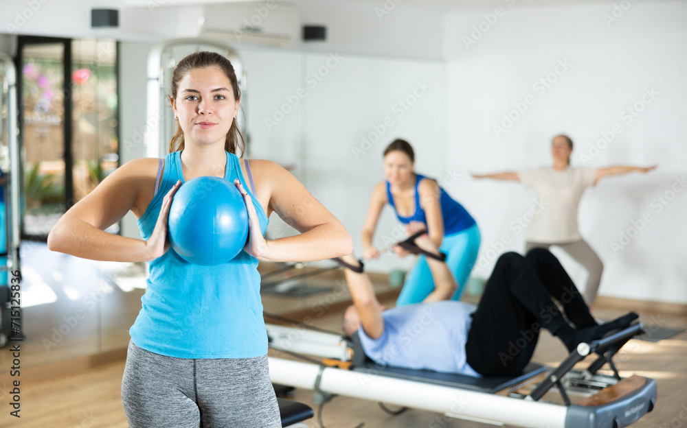 Smiling spotry young female squeezing ball in hands during Pilates training in modern fitness studio