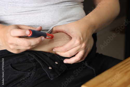 Woman applying insulin with insulin pen in her abdomen sitted in a chair. Woman with open jeans applying insulin 