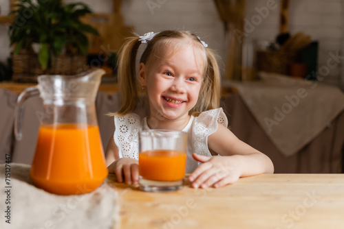 Cute little blonde girl drinking fresh orange juice in the kitchen