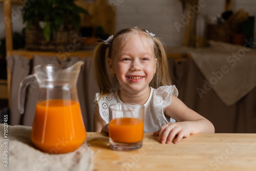 Cute little blonde girl drinking fresh orange juice in the kitchen