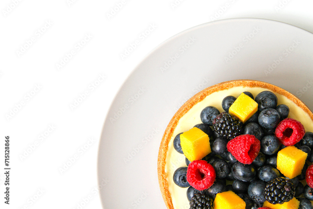 Cheesecake decorated with fresh berries and mango. On a light gray plate. White background. Top view. There is a copy space for your text. Cheesecake decorated with fresh berries and mango. On a light gray plate. White background. Top view. There is a copy space for your text.