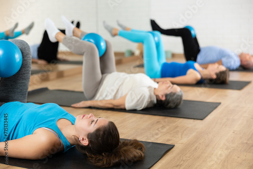 Positive young girl performing set of exercises with bender ball during group pilates class in fitness studio