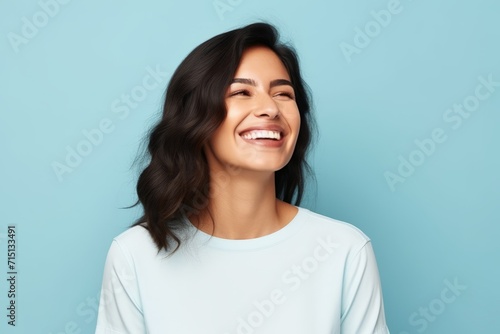 Portrait of a happy young woman laughing and looking up over blue background