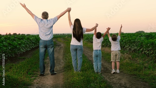 Joyful family with kids raises hands standing in meadow during summer break. Delighted family and kids relish being together in natural park on vocation. Children with family raise hands in unison
