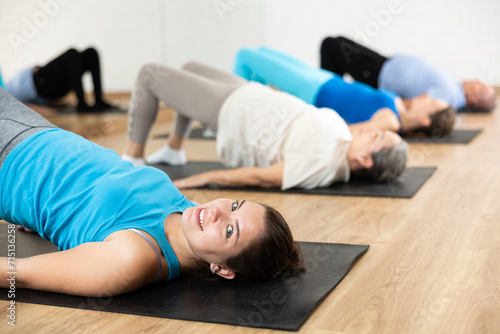 Class of male and women of different ages in active wear doing buttock bridge exercise during Pilates training together in gym