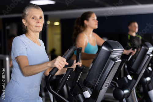 Mature female athlete working out at elliptical machine in gym