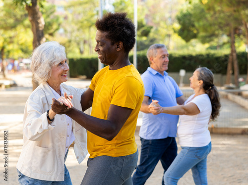 A troupe of cheerful multiracial amateur dancers of different age performing a partner dance outdoors in city park with one couple dancing in the foreground and the other behind © JackF