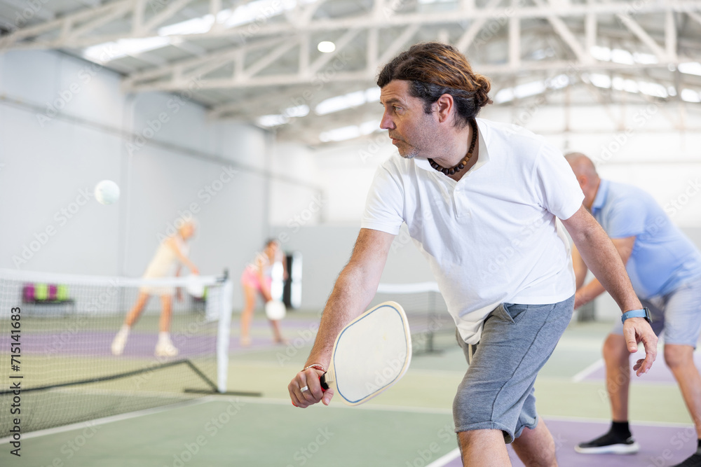 Athletic men playing pickleball tennis on the pickleball court indoors