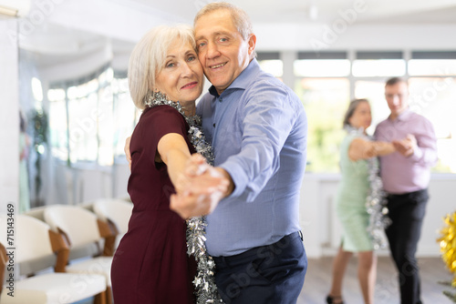 фотографія Against background of Christmas tree and decorations in studio, elderly couple enthusiastically dances rock and roll