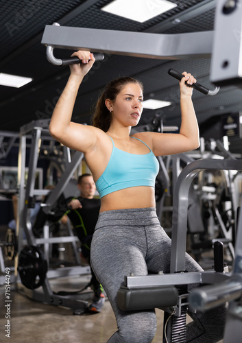 Emotional athletic young girl working out on lat pulldown lever machine, performing back exercises. Fitness and weight training concept