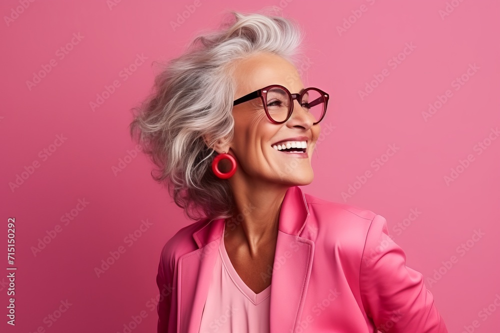 Portrait of a happy senior woman in glasses over pink background.