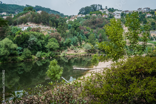 Green leafy bushes framing the Mondego river with wooden bridge in the valley with houses on the hill, Penacova PORTUGAL