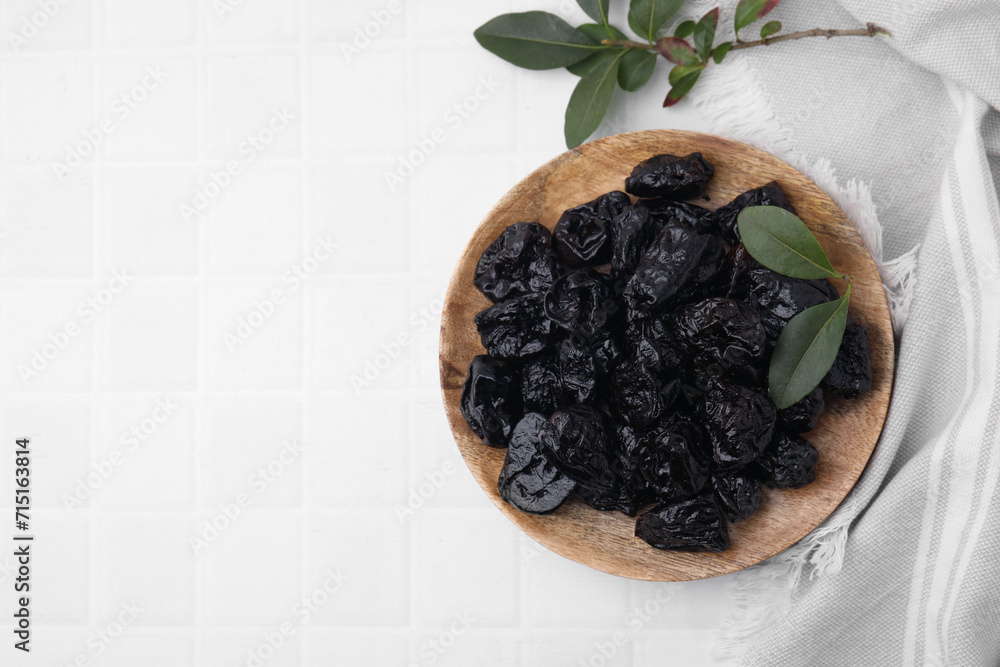 Sweet dried prunes and green leaves on white tiled table, top view. Space for text Sweet dried prunes and green leaves on white tiled table, top view. Space for text