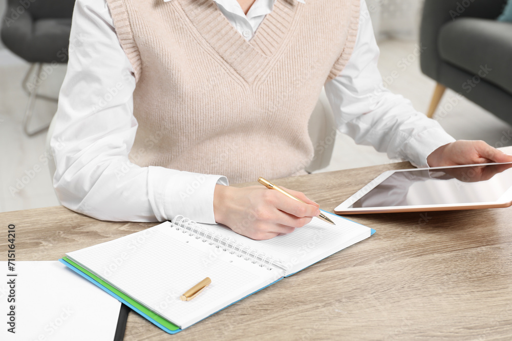 Woman taking notes while using tablet at wooden table in office, closeup Woman taking notes while using tablet at wooden table in office, closeup