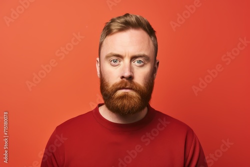 Surprised bearded man looking at camera. Studio shot over red background.