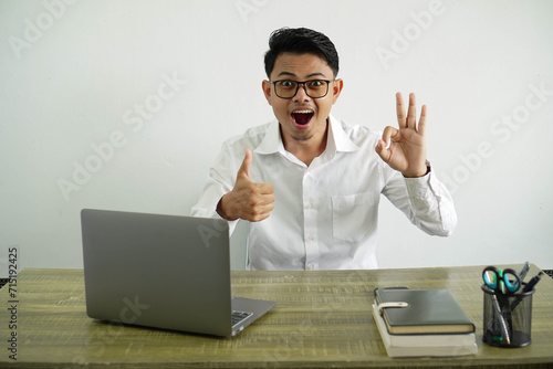 Canvas Print young asian businessman in a workplace showing ok sign and thumb up gesture, wea