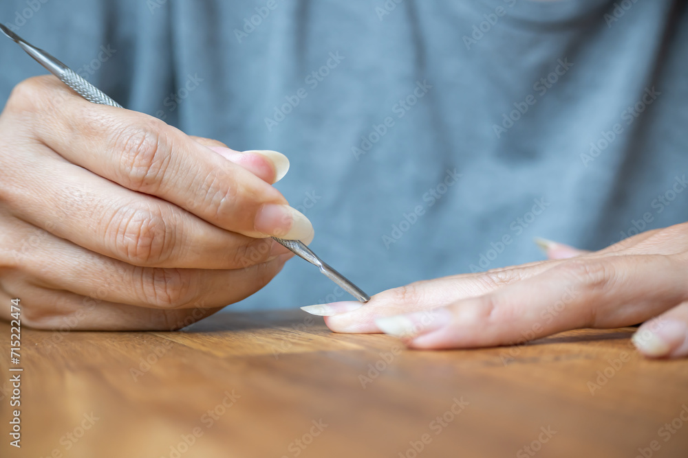Woman using a cuticle pusher on her nails. Nail preparation process before applying polish. - obrazy, fototapety, plakaty 