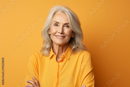 Portrait of smiling senior woman looking at camera over yellow background.