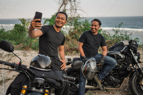 asian men sitting on motorbike and taking picture together using handphone © Odua Images