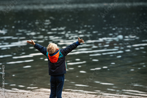 Child on the edge of a lake arms up feeling happy and free in nature 