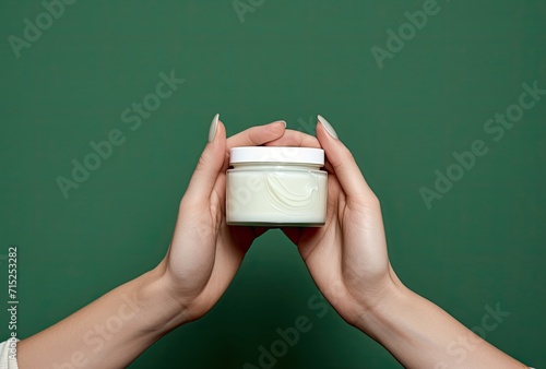Female hands elegantly holding a jar of moisturizer cosmetic cream against a fresh green background, emphasizing skincare and natural beauty.