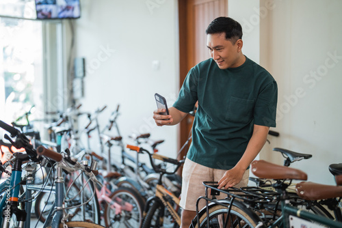 young man takes pictures of some new bicycles using a cell phone camera at a bicycle shop