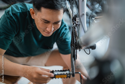 handsome young man repairing bicycle pedal with allens key in bicycle shop photo