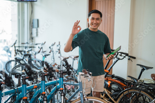 young entrepreneur smiles with an okay hand gesture holding a digital tablet at a bicycle shop