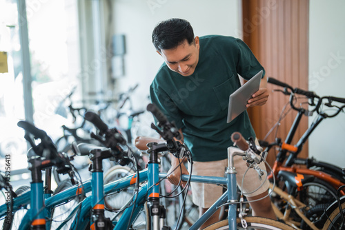 young man looking at a new bicycle frame while using a tablet at a bicycle shop