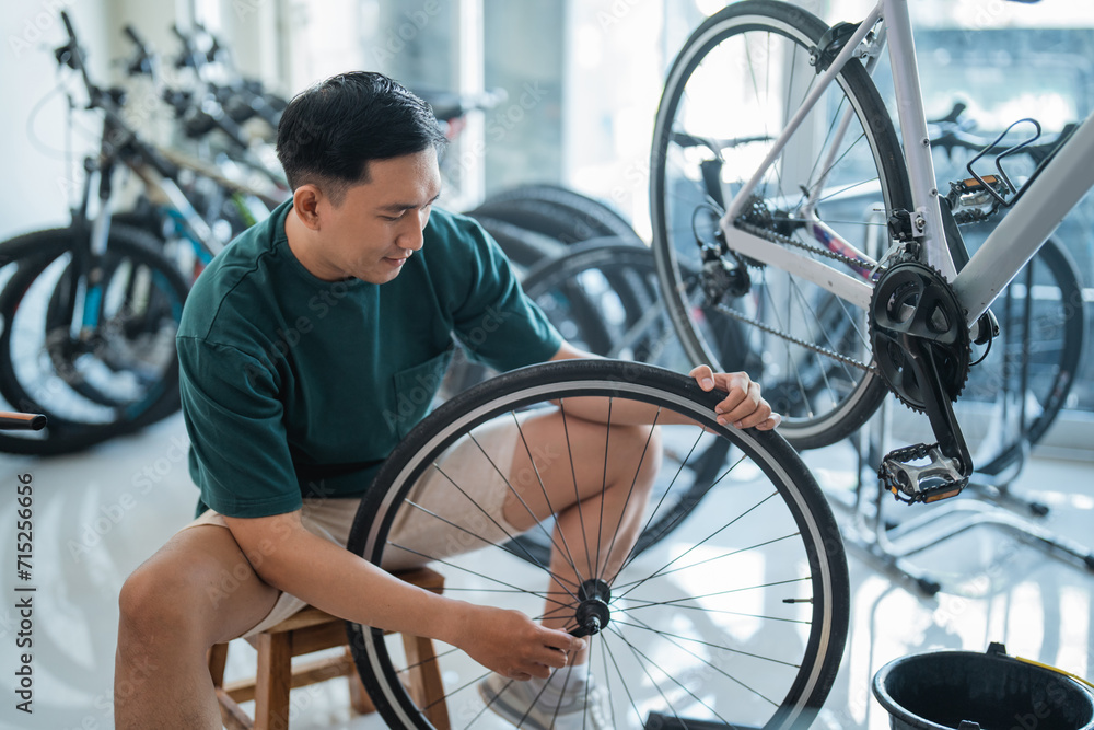 young Asian man repairs axles while working in a bicycle shop - obrazy, fototapety, plakaty 