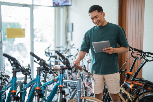 young man checks the handlebars of a bicycle while using a tablet at a bicycle shop