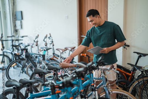 young man checks the saddle of a new bicycle while using a tablet at a bicycle shop