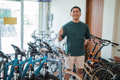 smiling entrepreneurial man with thumbs holding a digital tablet in a bicycle shop