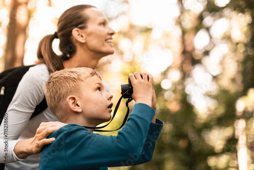 Mother child together hiking in the forest looking through binoculars bird watching exploring learning about nature, family adventure  photo