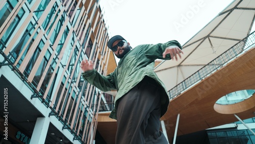 Low angle view of hipster pose in hip hop style surrounded by mall view. Portrait of sporty asian hip hop choreographer dancing break dance while looking at camera. Outdoor sport 2024. Endeavor. photo