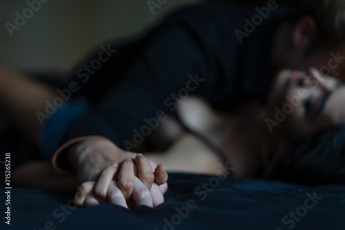 Man's hand holding a woman hand for rape and sexual abuse concept. Couple in love holding hands tight in bed close-up touching each other on a black blanket, enjoying honeymoon, valentine's day