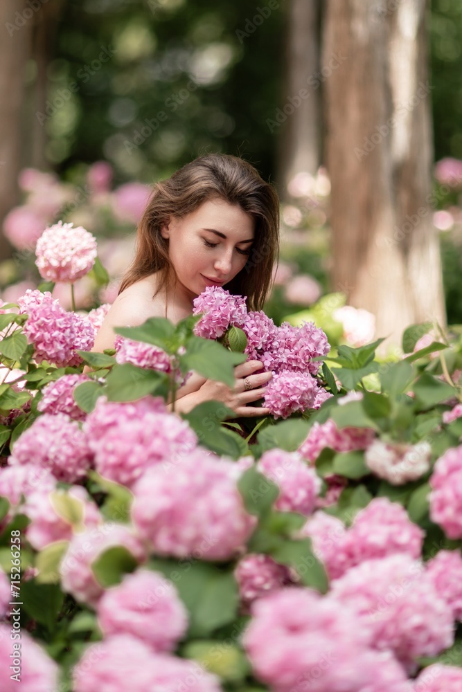 Hydrangeas Happy woman in pink dress amid hydrangeas. Large pink hydrangea caps surround woman. Sunny outdoor setting. Showcasing happy woman amid hydrangea bloom. Hydrangeas Happy woman in pink dress amid hydrangeas. Large pink hydrangea caps surround woman. Sunny outdoor setting. Showcasing happy woman amid hydrangea bloom.