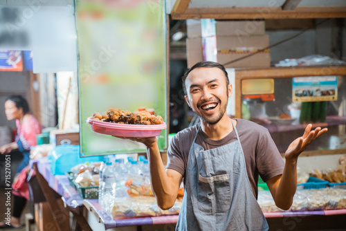 smiling Asian youth wearing an apron with one hand holding a side dish at a traditional stall photo
