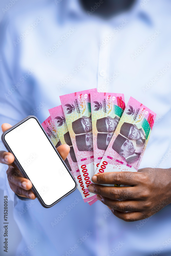 Black person holding Indonesian rupiah notes and showing mobile phone with blank screen to the camera. Hand holding Indonesian currency notes, 3d rendered money Black person holding Indonesian rupiah notes and showing mobile phone with blank screen to the camera. Hand holding Indonesian currency notes, 3d rendered money