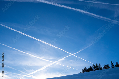 Contrails in the blue sky.  Mountain landscape with snow and tree silhouette