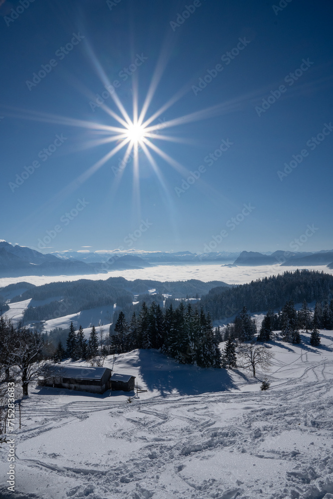 Beautiful winter landscape. View from a mountain (Spitzstein) on the German-Austrian border of a blanket of fog over the Inn Valley. A ski slope and a farmhouse, blue sky with star-shaped glare
