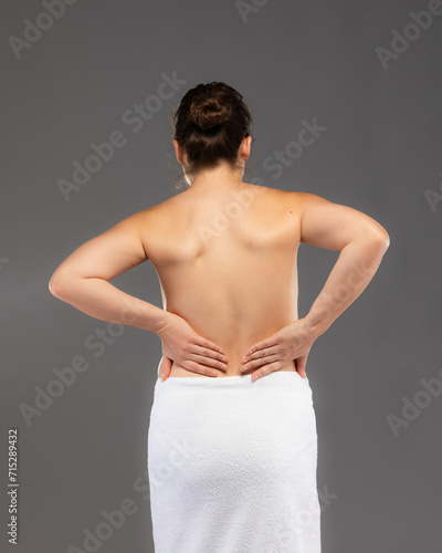 Young woman massaging back pain on gray background 