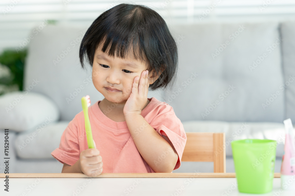little asian girl presses hand to cheek, suffers from pain in tooth. Teeth decay, dental problems, child emotions and facial expression, oral health care, reducing sweets, fluorine coating. little asian girl presses hand to cheek, suffers from pain in tooth. Teeth decay, dental problems, child emotions and facial expression, oral health care, reducing sweets, fluorine coating.