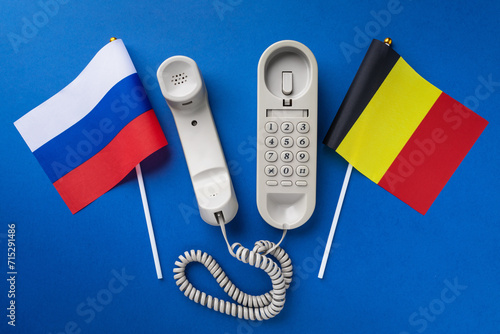 Old telephone and two flags on a blue background, concept on the theme of telephone conversations between Belgium and Russia